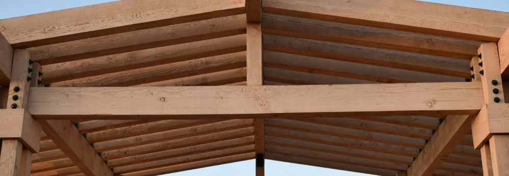 Nahaufnahme einer Dachkonstruktion aus Holz vor blauem Himmel.